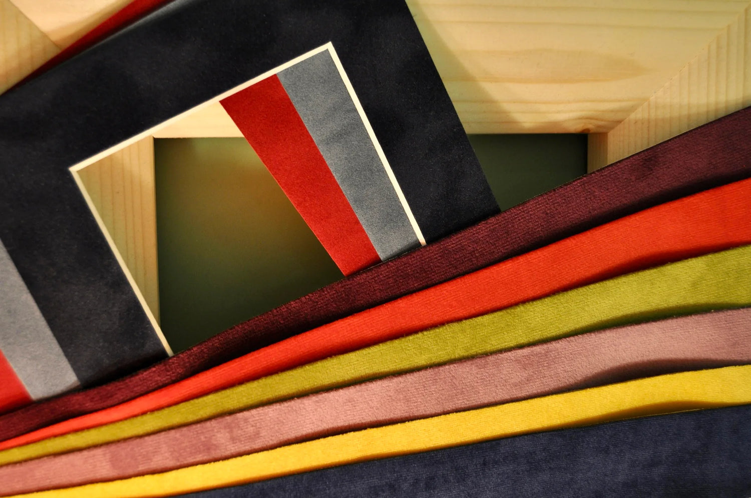 Ein unbezogener Holzrahmen, darüber Passepartouts und Samt-Streifen in kräftigen Farben, die später als Inlays verarbeitet werden. Das Bild zeigt einzelne Komponenten des Rahmendesigns in der Entstehung.