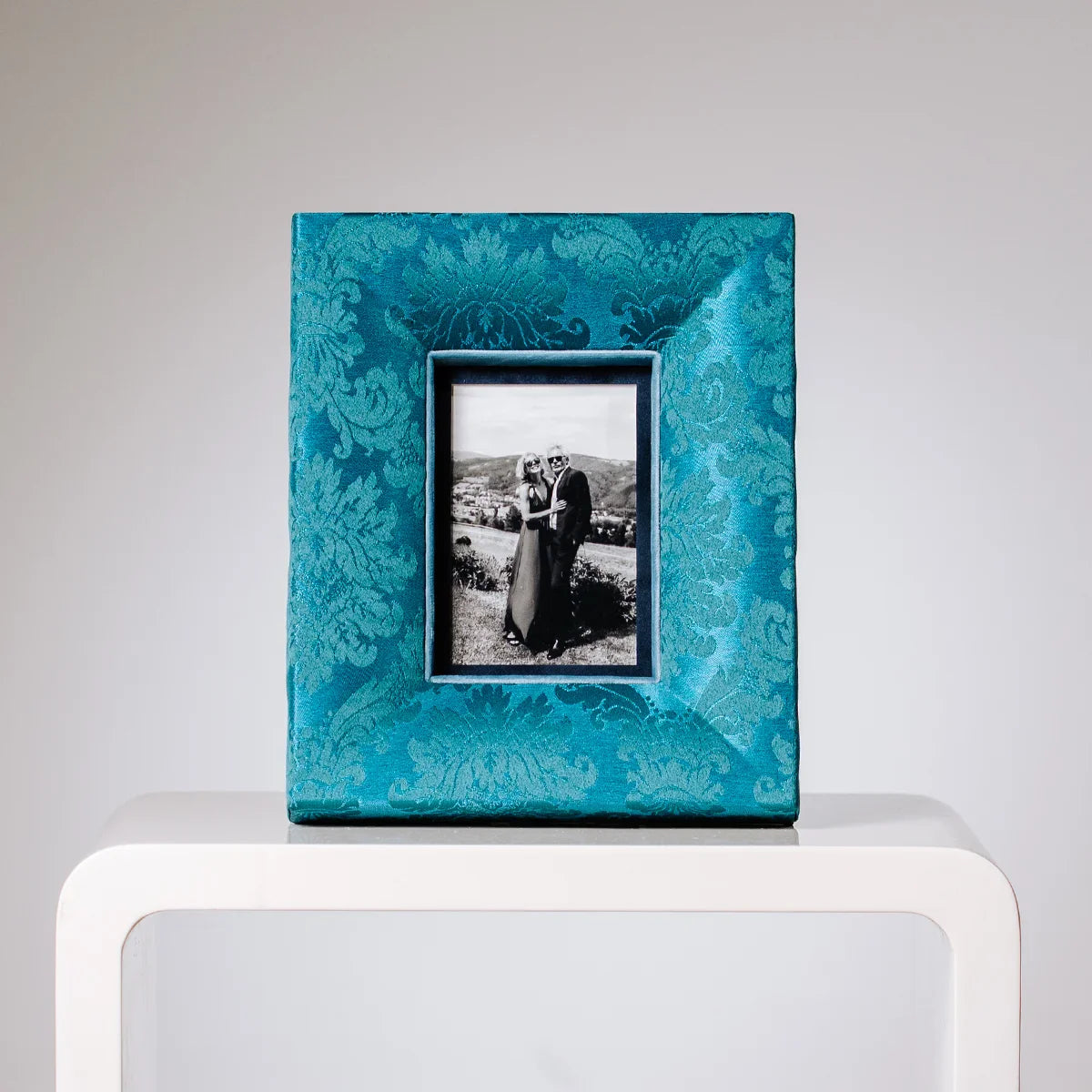 Handgemachter türkisblauer Stoffbilderrahmen mit floralem Muster, eingerahmtes schwarz-weißes Hochzeitsfoto eines Paares.