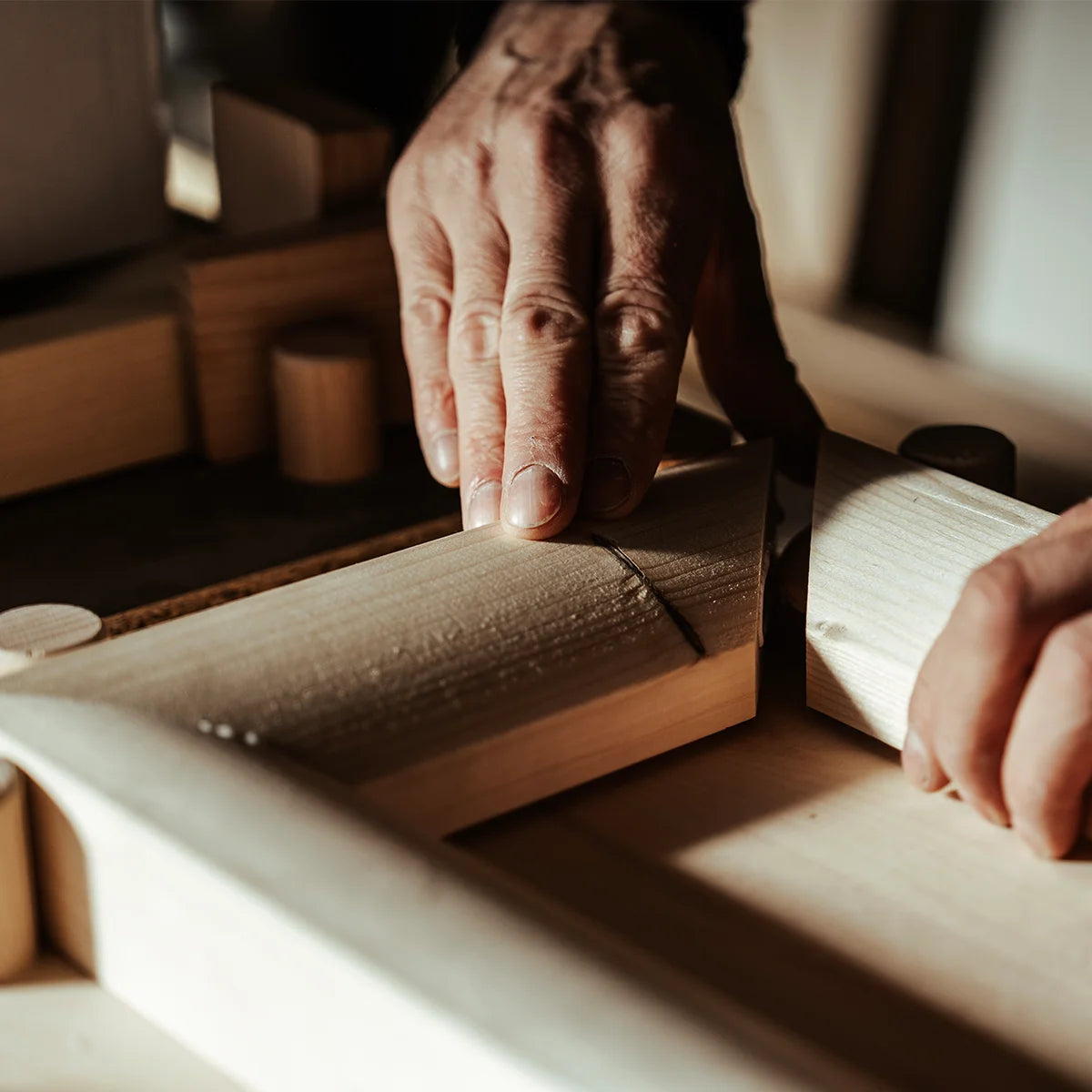 Hände eines Tischlers richten einen massiven Holzrahmen präzise aus. Herstellung eines handgefertigten Design-Bilderrahmens aus Holz, gefertigt in Österreich bei PIC | PUNK.