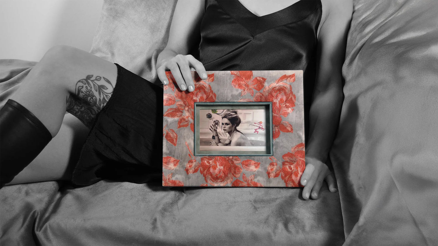 Schwarzweiß-Fotografie einer Frau auf einem Sofa, die einen handgefertigten Design-Bilderrahmen von PIC | PUNK mit rotem Blumenmuster und Porträt hält – modernes Statement Design für außergewöhnliche Wohnräume.