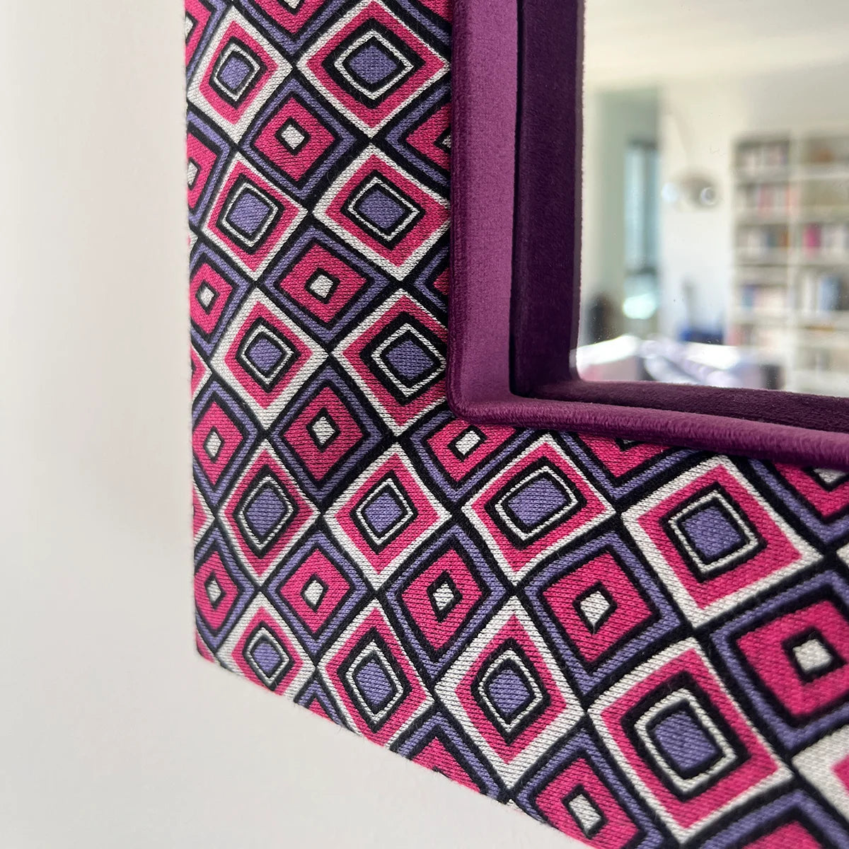 Detail eines handgefertigten Wandspiegels mit lila und pinkem Stoffrahmen und buntem Rautenmuster im Retro-Stil.
